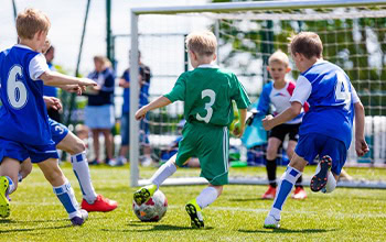 amateur youth soccer player in green dribbling past two opponents in blue uniforms during a match