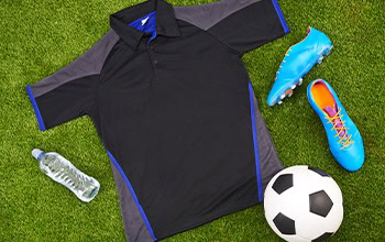 a black, grey, and blue soccer polo with bright blue and orange soccer cleats, and a soccer ball laying on the ground